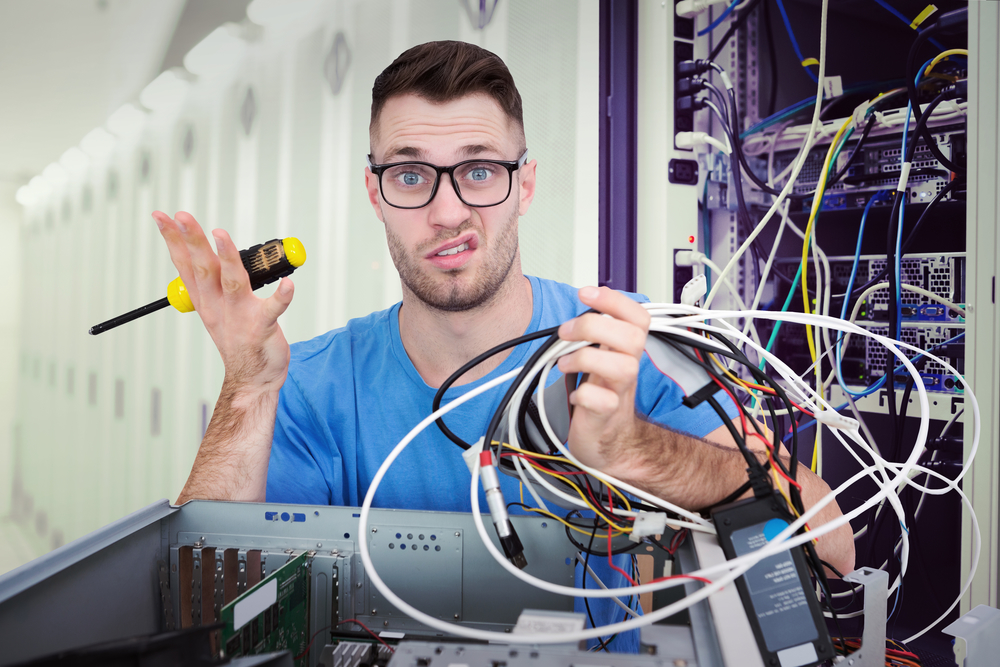 Portrait of confused it professional with screw driver and cables in front of open cpu against data center